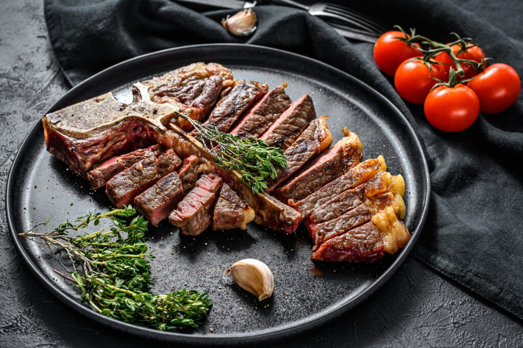 Grilled Porterhouse steak on a chopping Board. Cooked beef meat. White wooden background. Top view