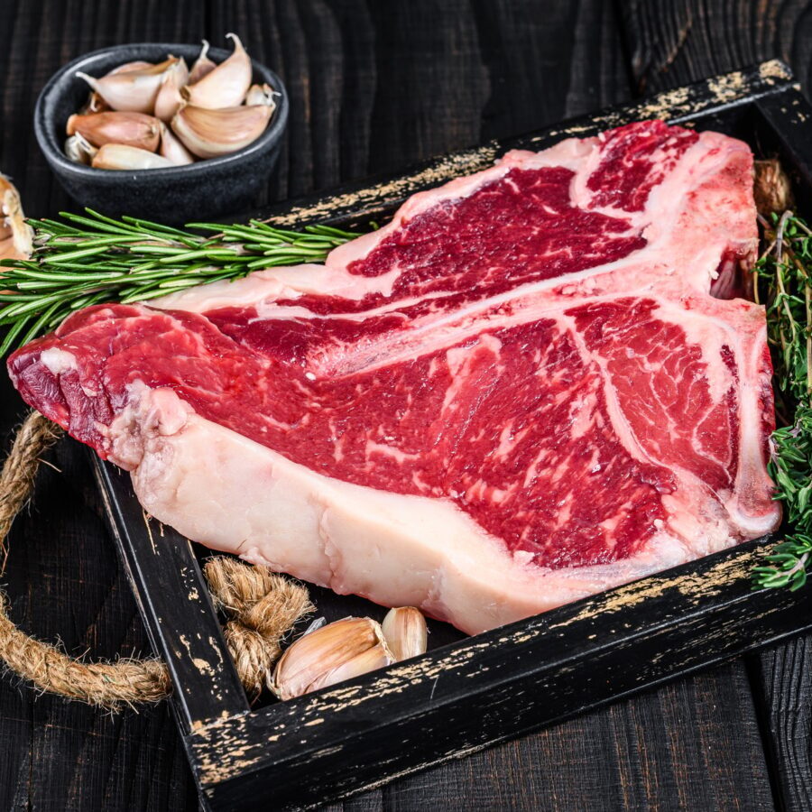 Porterhouse or T bone raw beef meat Steak with herbs and salt in wooden tray.