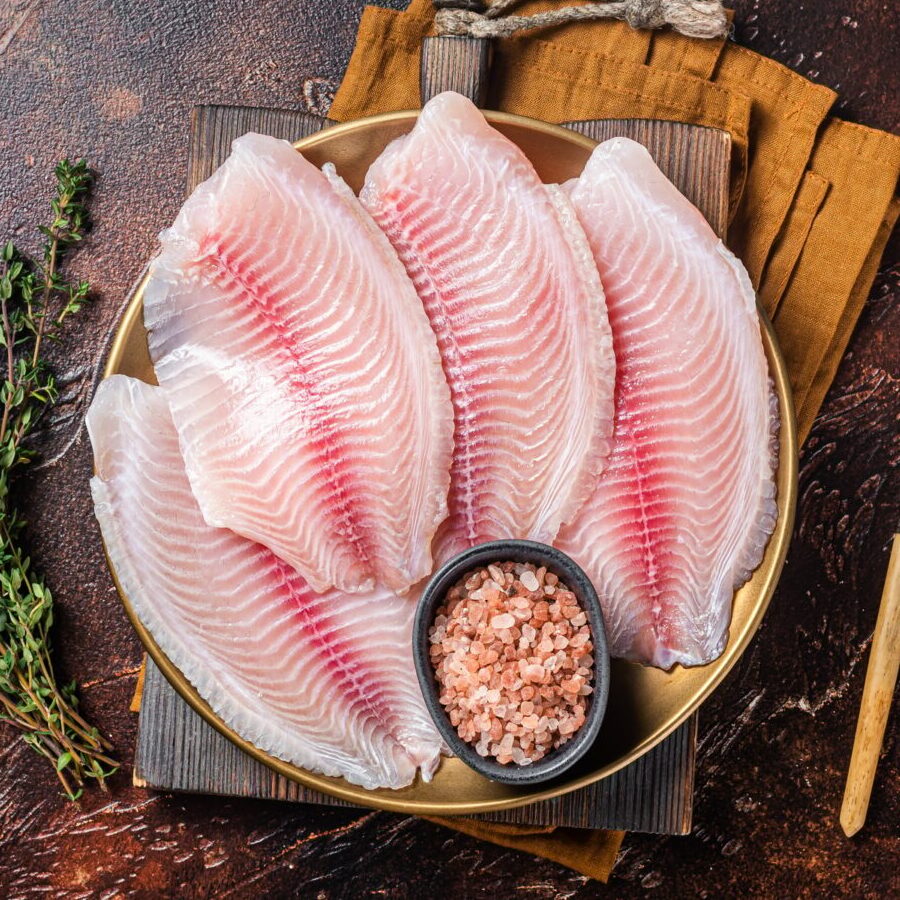 Raw fish fillet of tilapia in a plate with spices. Dark background. Top view