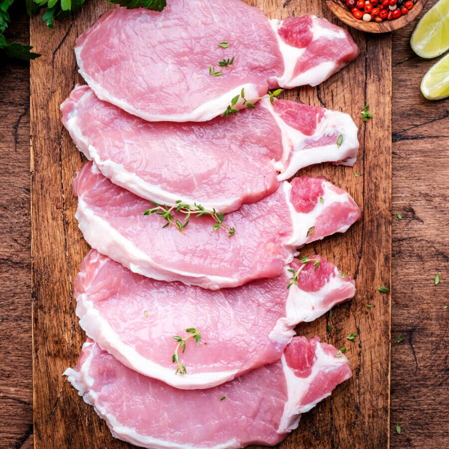 Raw pork chops on wooden board prepared for cooking with spices and pepper. Wood kitchen table