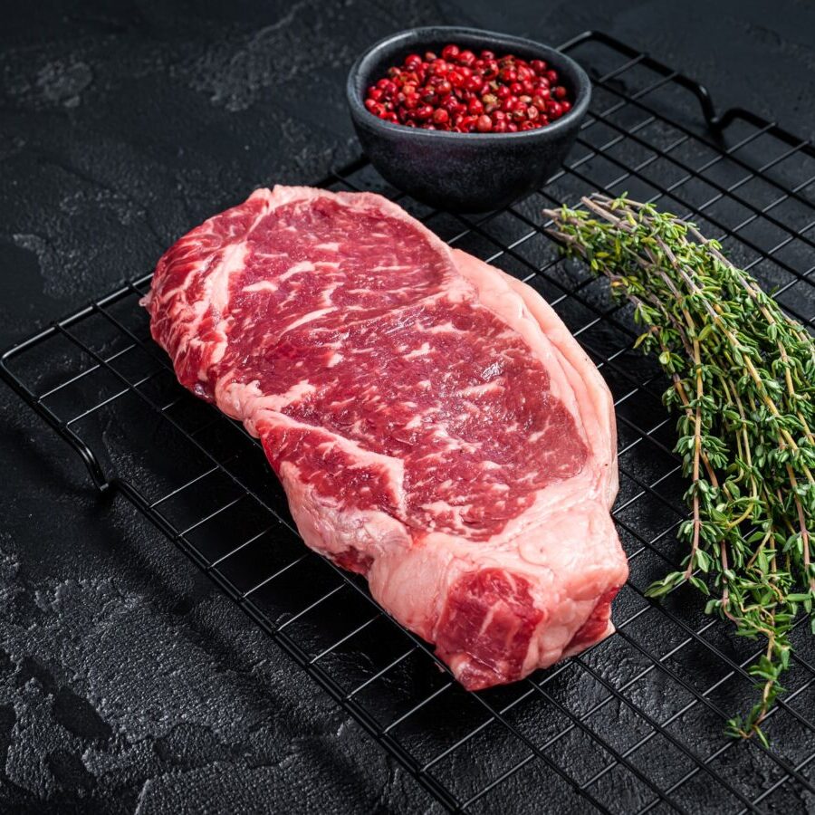 Raw striploin or New York beef meat steak ready for BBQ. Black background. Top view. Copy space